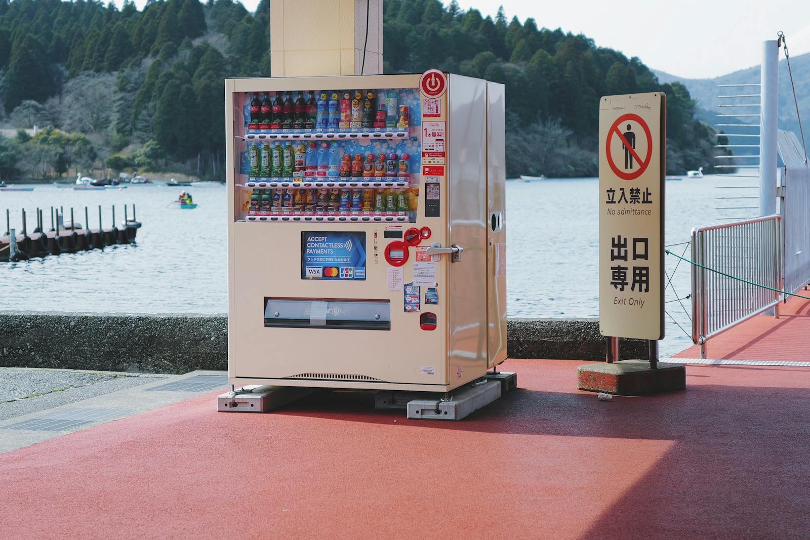 Vending machine by a lakeside sidewalk with scenic view.